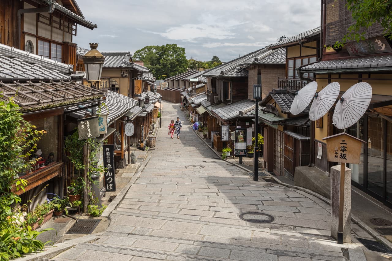 People in summer yukata walking a paper-umbrella-lined street in Higashiyama, Kyoto